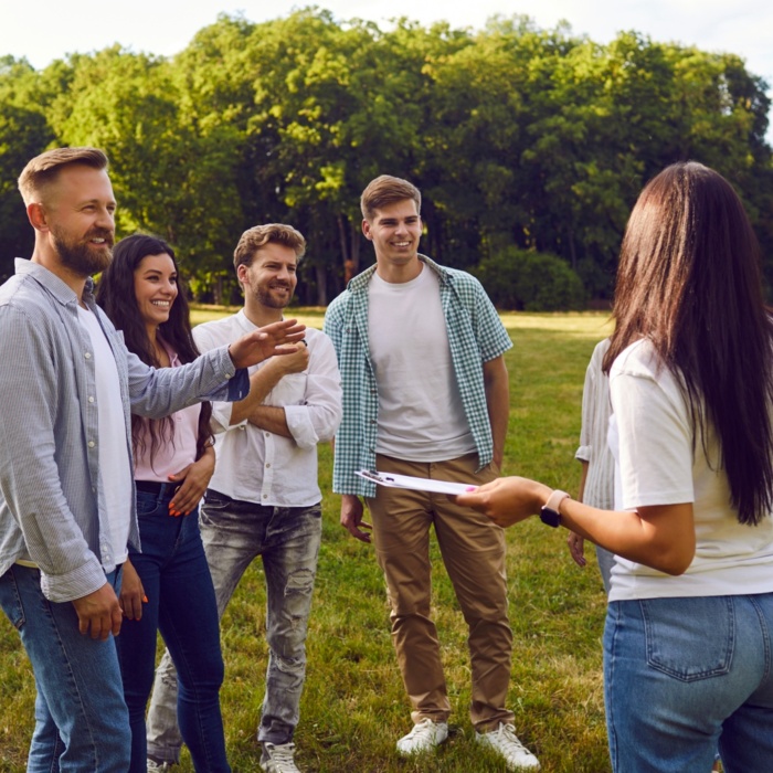 Grupa sześciu osób bawiących się na świeżym powietrzu w słonecznym parku z zielonymi drzewami w tle
