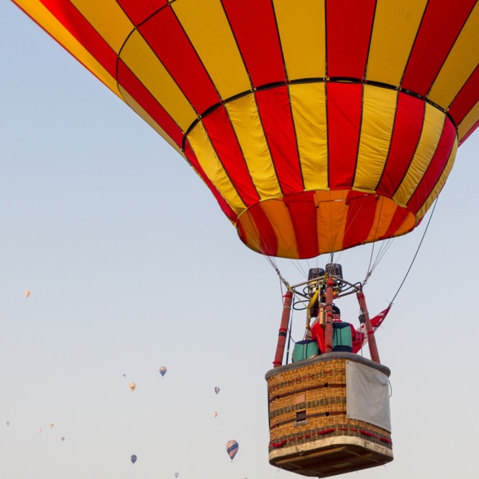 Kolorowy balon na gorące powietrze unosi się na tle bezchmurnego nieba z wieloma innymi balonami w oddali