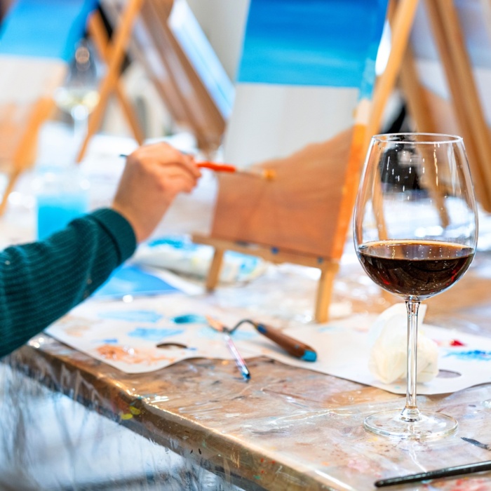 Goście biorący udział w warsztatach malarskich z kieliszkiem czerwonego wina i napojem na stole