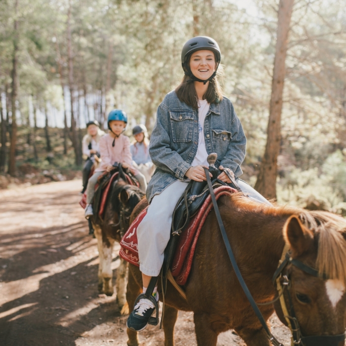 Grupa dzieci na koniach podczas wycieczki po leśnej ścieżce w słoneczny dzień w ośrodku jeździeckim