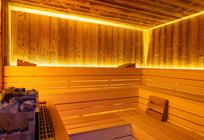 Przytulna sauna z drewnianymi ławami, kamieniami do sauny i ciepłym, nastrojowym oświetleniem LED