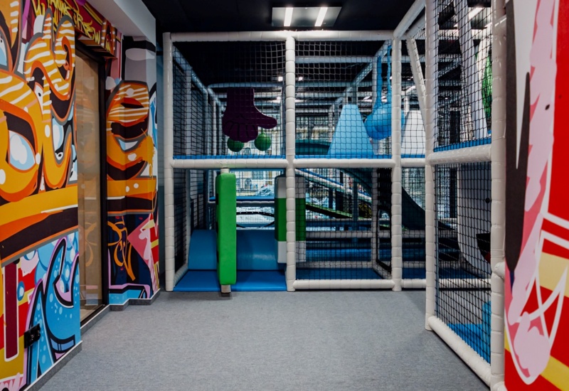 Kolorowy, bezpieczny plac zabaw dla dzieci w hotelu, z miękkimi przeszkodami i ścianami pokrytymi muralami graffiti.