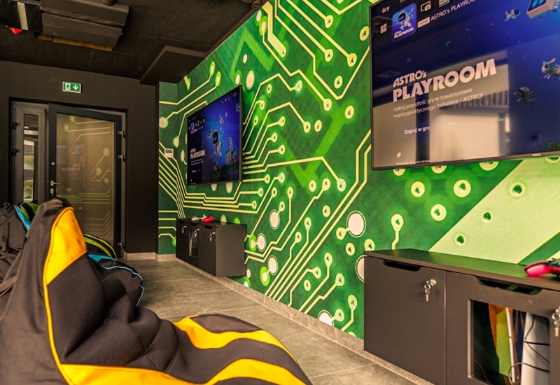 Pokój do gier z wygodnymi pufami, dużymi ekranami TV i ścianą ozdobioną wzorem obwodów elektronicznych