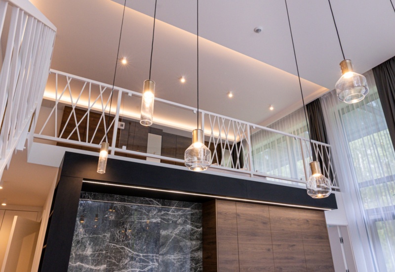 Nowoczesne wnętrze hotelowe z antresolą, designerskimi lampami wiszącymi i dużymi oknami z delikatnymi zasłonami.