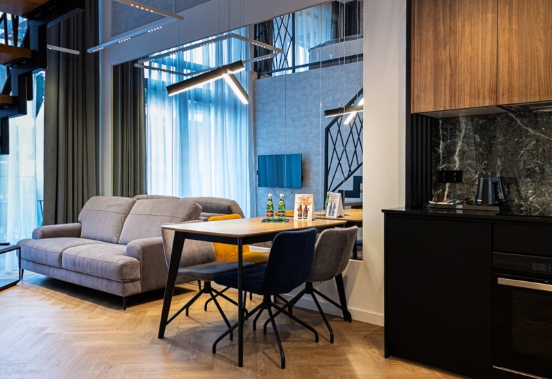 Nowoczesny apartament z dwupoziomowym wnętrzem, szarą sofą, jadalnią na cztery osoby i aneksem kuchennym z czarnym marmurem