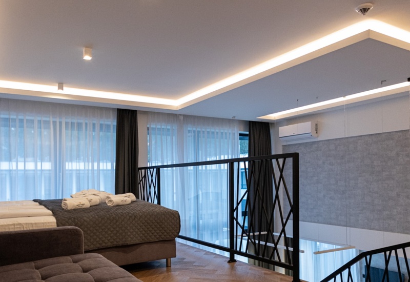 Nowoczesny apartament typu loft z dużym łóżkiem, sofą, ozdobnym oświetleniem i przeszklonym balkonem z widokiem na dół