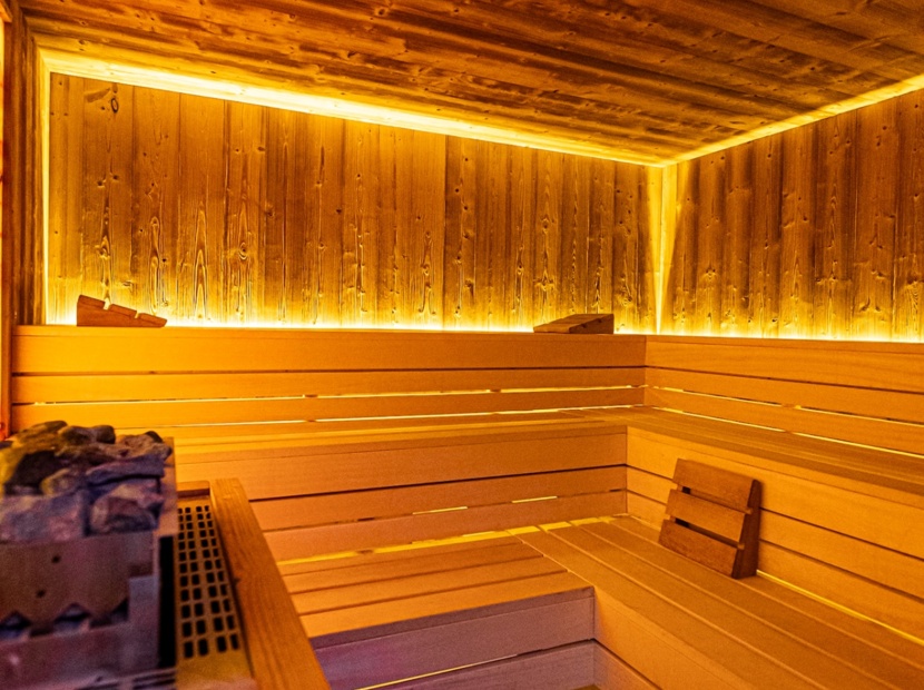 Przytulna sauna z drewnianymi ławami, kamieniami do sauny i ciepłym, nastrojowym oświetleniem LED