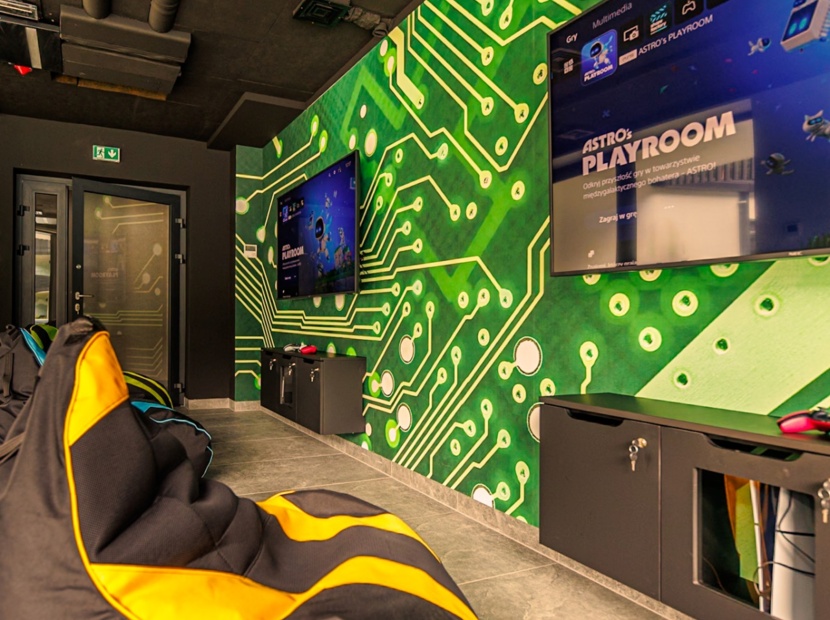 Pokój do gier z wygodnymi pufami, dużymi ekranami TV i ścianą ozdobioną wzorem obwodów elektronicznych