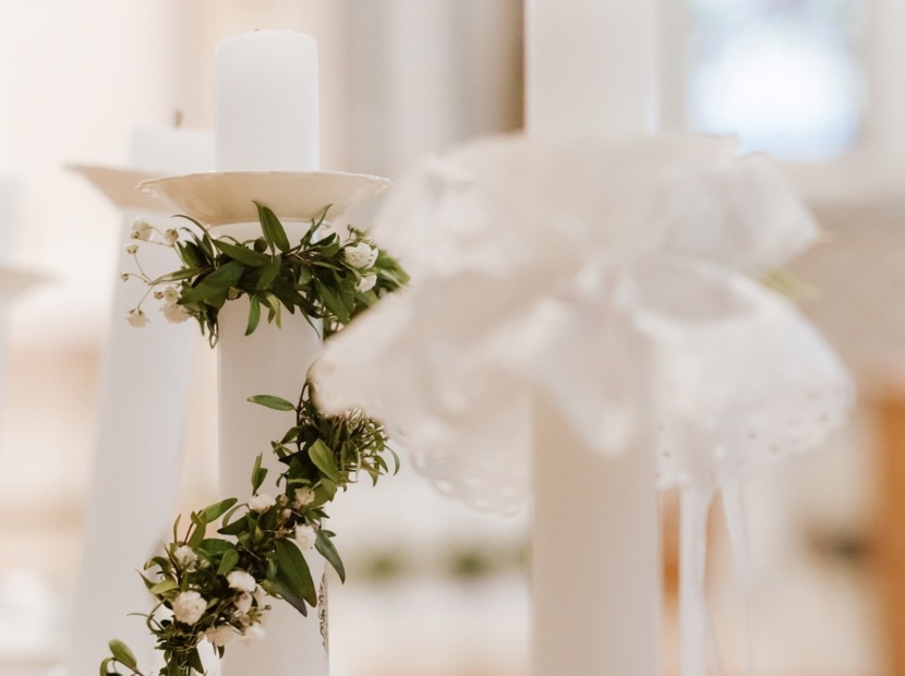 Białe ozdobne świece z delikatnym wieńcem zielonych liści i małych białych kwiatów, tworzące elegancką dekorację