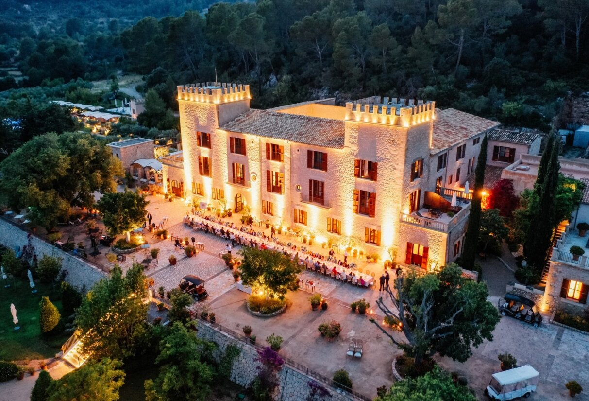 Beleuchtetes Schlosshotel auf Mallorca mit großen Tischen im vorderen Bereich für eine große Feier