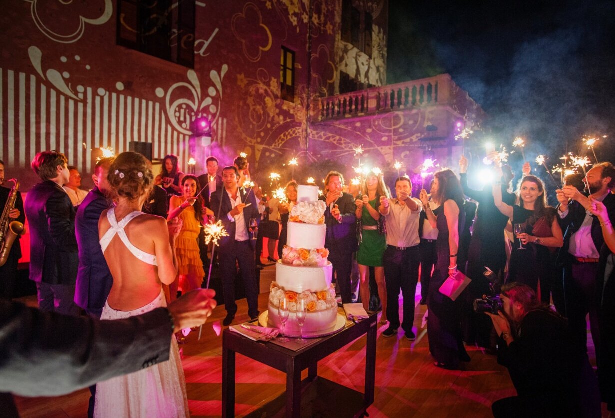 Una fiesta en una boda en mallorca con una pareja de novios delante de una gran tarta y los invitado