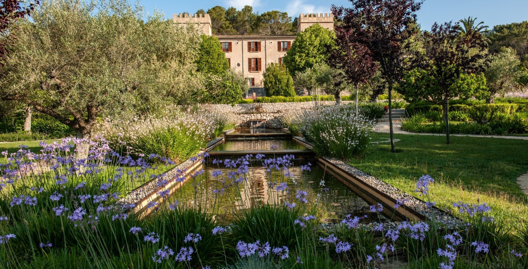 Ein Schlosshotel auf Mallorca mit zwei Türmen an der Seite und einem Teich im Garten
