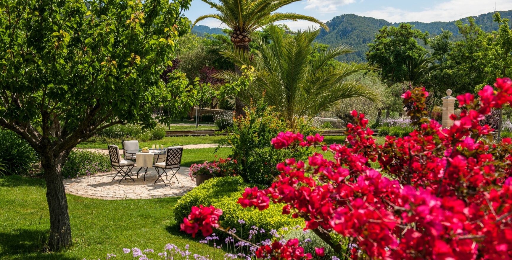 Ein sonniger Hotelgarten auf Mallorca mit einem Tisch und roten Blumen an der Seite