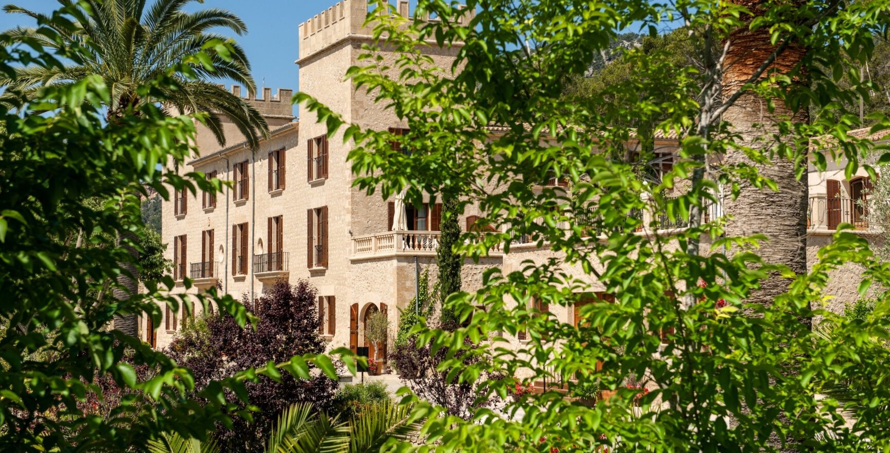 Grüne Bäume vor einem Schlosshotel auf Mallorca mit hellen Steinmauern