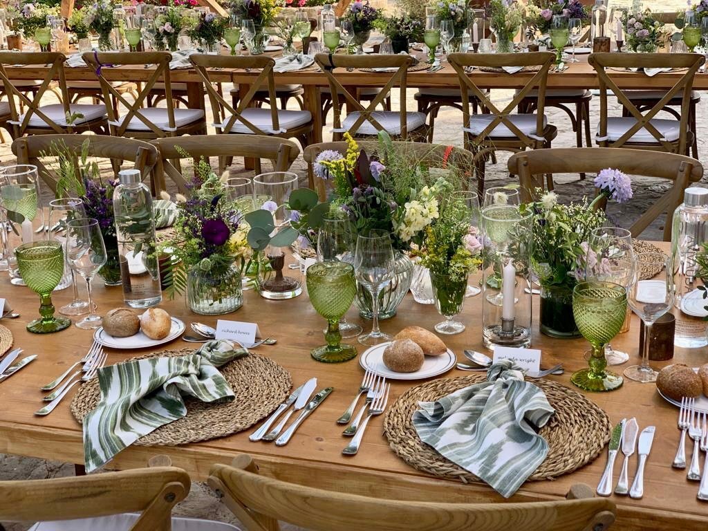 Gedeckte Tische für eine Hochzeit mit Blumen in der Mitte, geflochtenen Untersetzern und etwas Brot