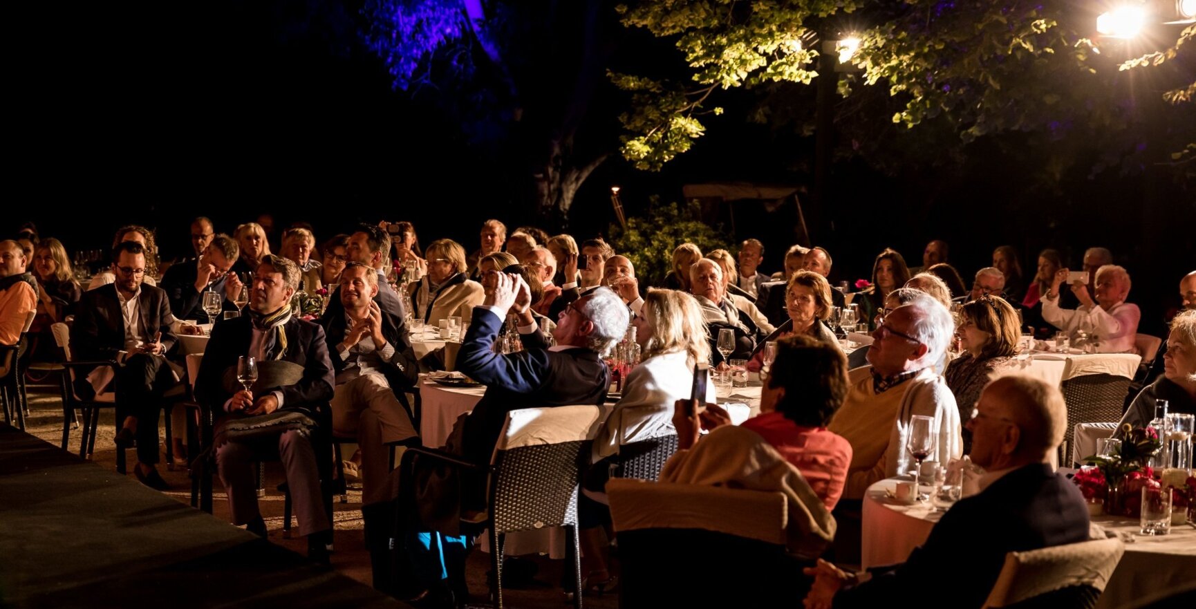 Hotelgäste sitzen im Dunkeln an Esstischen im Freien und sehen sich eine Show an