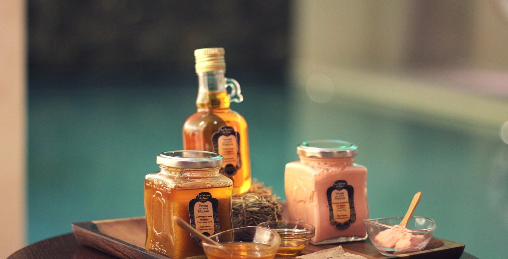 Productos de spa variados en frascos y botellas de vidrio sobre bandeja de madera, en ambiente relajante de spa con luz suave