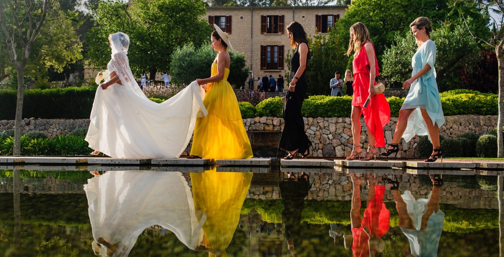 Bridesmades están caminando con una novia por un estanque en un hermoso lugar de bodas en mallorca