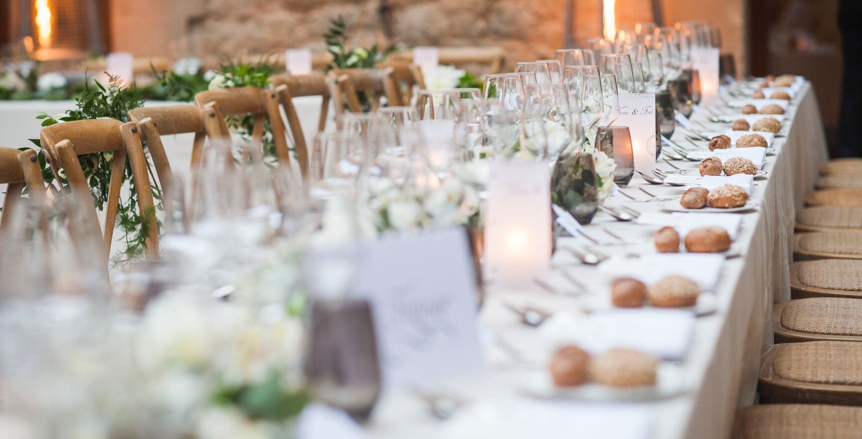 Mesa larga en una boda en Mallorca con pan, copas de vino y algunas plantas verdes