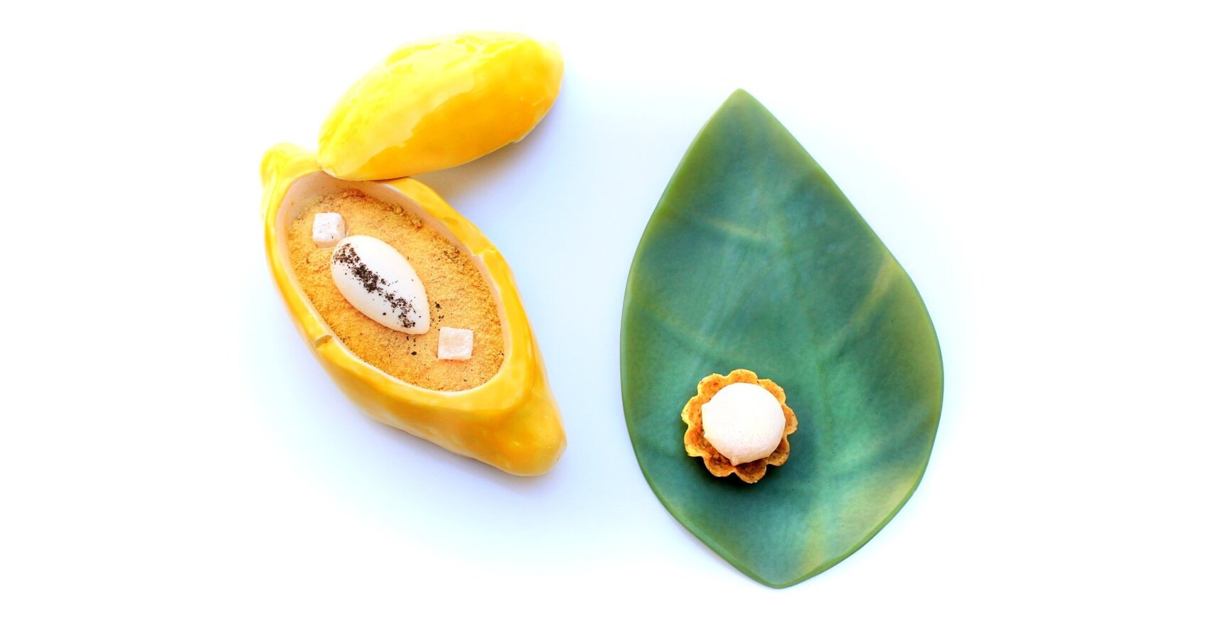 Feines Gourmet-Dessert mit Creme und Bröseln in gelber Schotenform sowie kleines Törtchen auf grünem Blatt-Teller