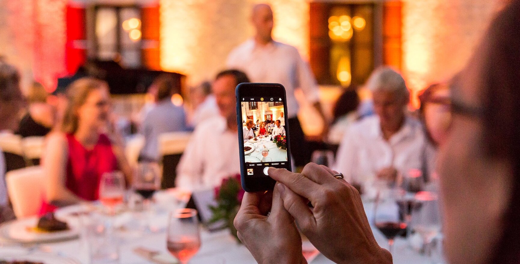 Gäste genießen ein elegantes Abendessen im Freien in einem warm beleuchteten Veranstaltungsort mit Weingläsern und servierten Speisen