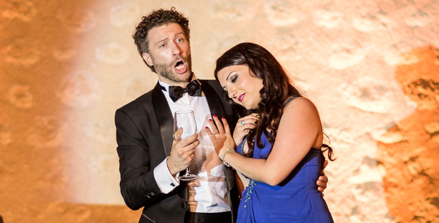 Mann im Smoking singt leidenschaftlich mit einer Frau in elegantem blauem Kleid bei einer Gala