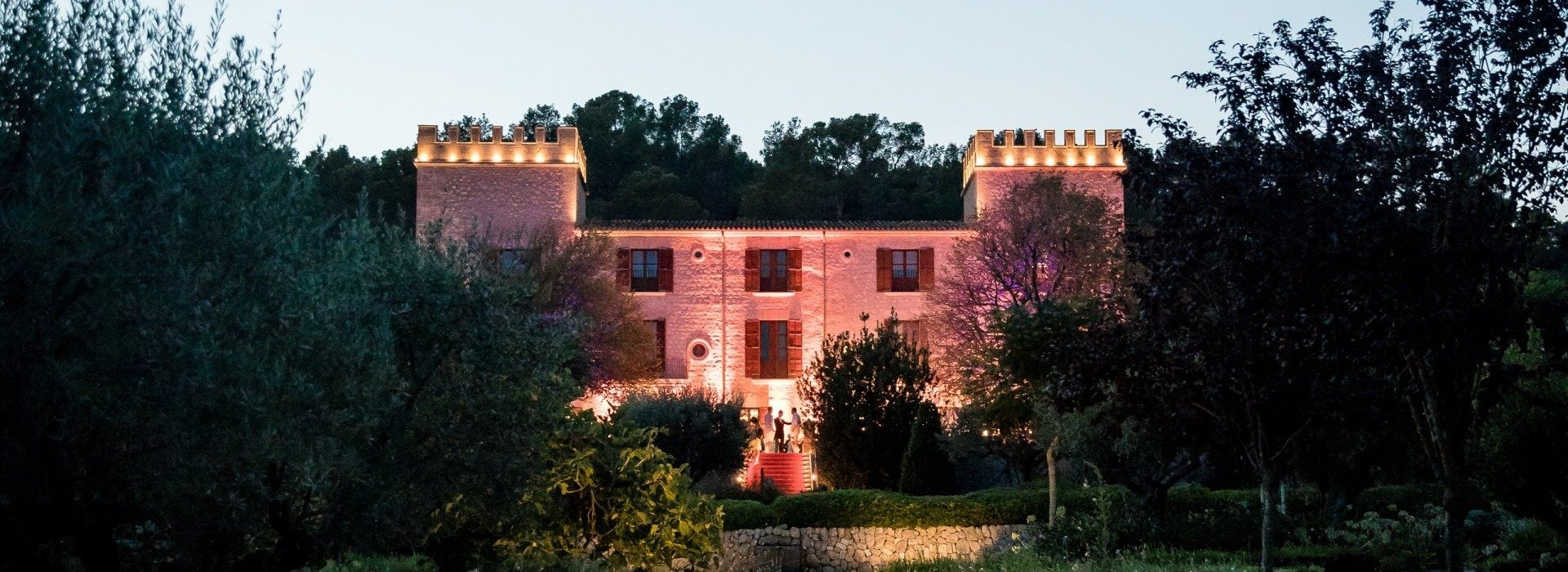 Beleuchtetes Schlossgebäude eines Hotels auf Mallorca mit einem Garten und einem Teich davor