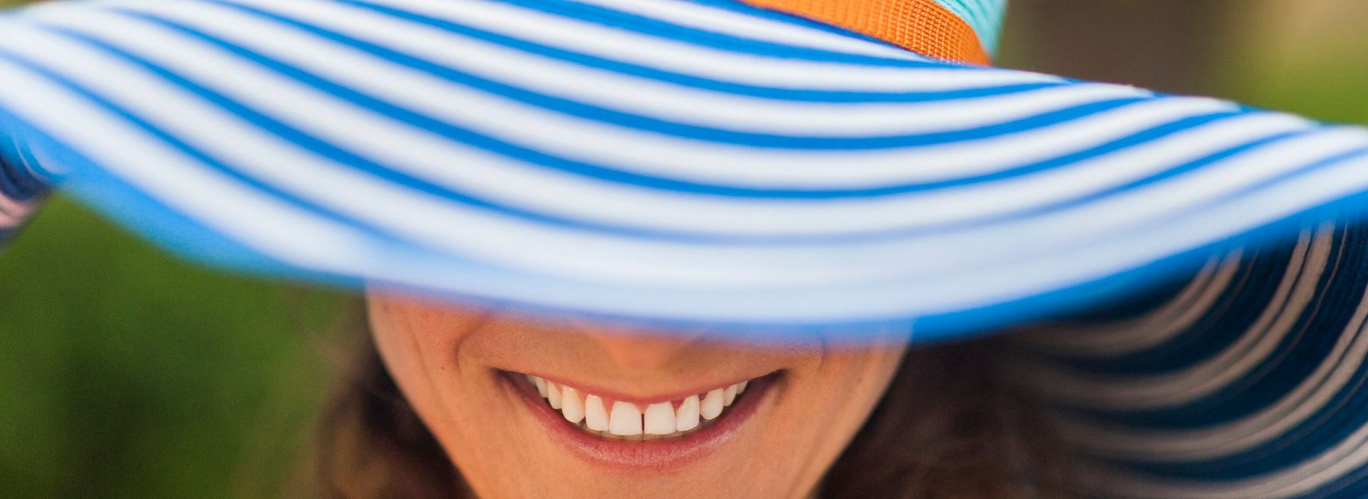 Smiling guest wearing a colorful wide-brimmed sun hat, enjoying a sunny outdoor hotel setting