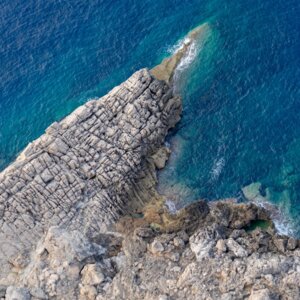 Luftaufnahme einer zerklüfteten felsigen Küste, die auf klares, tiefblaues Meer trifft