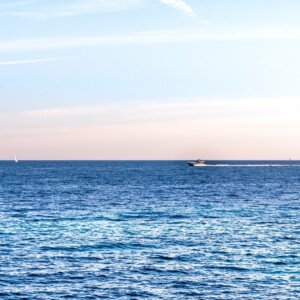 Ruhiger blauer Ozean mit einem Schnellboot und wenigen Segelbooten unter einem pastellfarbenen Abendhimmel