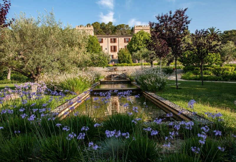 Ein Schlosshotel auf Mallorca mit zwei Türmen an der Seite und einem Teich im Garten