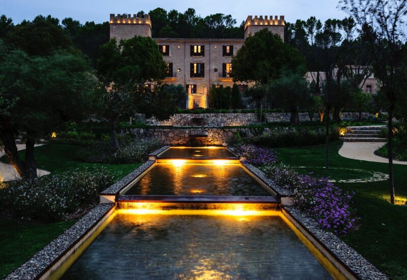 Elegante villa de piedra con cascadas iluminadas y jardines exuberantes con flores moradas al anochecer