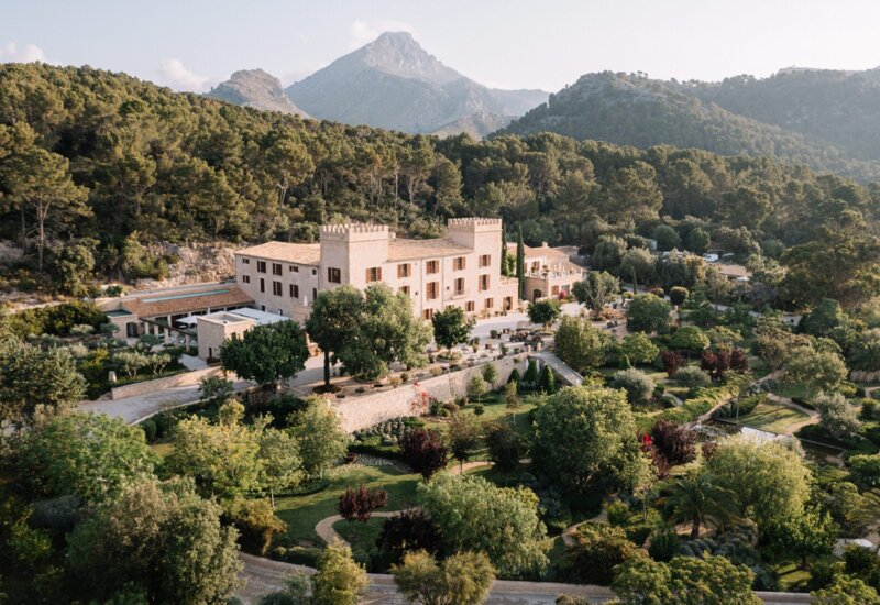 Historisches Steinhotel mit burgähnlichen Türmen, umgeben von üppigen Gärten und Bergblick in ruhiger Natur