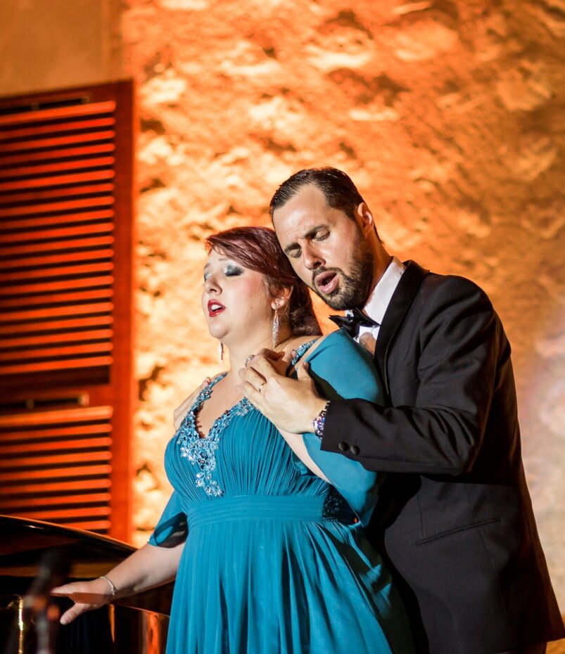 Two opera singers are standing together on stage and performing dramatically a song