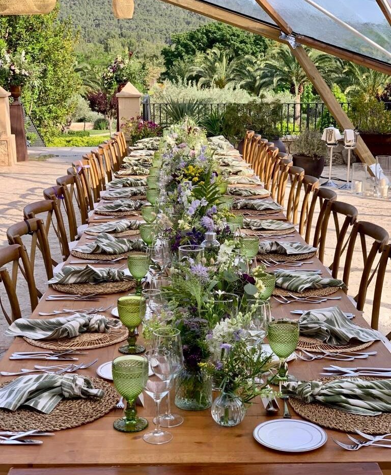 Langer Tisch, dekoriert mit grünen Gläsern, Handtüchern und vielen Blumen in der Mitte