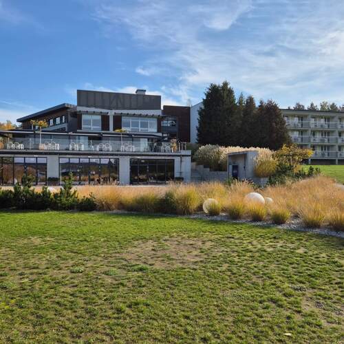 Nowoczesny hotel z rozległym trawnikiem, tarasem z szklanym balustradami i stolikami, ozdobnymi trawami i balkonami pokoi