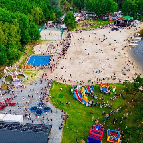 Plaża ośrodka z plenerową sceną, dmuchańcami i zjeżdżalniami, strefą rozrywki i łodziami przy brzegu