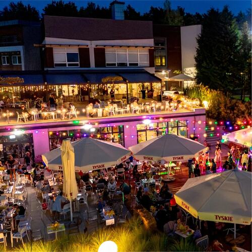 Dwupoziomowa tarasowa restauracja nocą, parasole TYSKIE, stoliki z gośćmi, kolorowe girlandy i nastrojowe światło