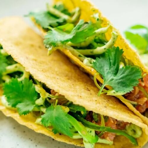 Dwa chrupiące tacos z kukurydzy z kremowym guacamole, salsą pomidorową i świeżą kolendrą — apetyczne danie restauracyjne
