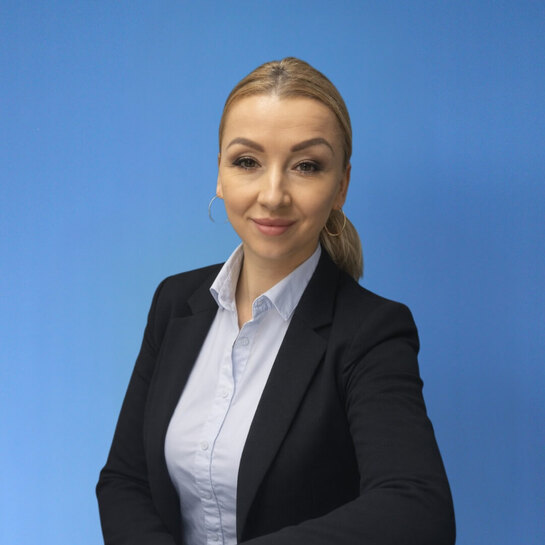 Uśmiechnięta pracownica recepcji w czarnym żakiecie i jasnej koszuli na niebieskim tle