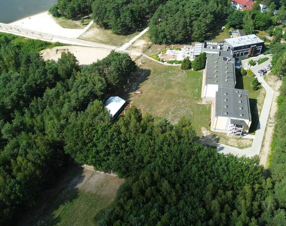 Hotel przy lesie i piaszczystej plaży z tarasem zewnętrznym, ścieżkami spacerowymi, parkingiem i pomostem nad jeziorem.