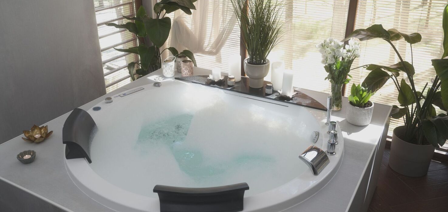 Jacuzzi z bąbelkami i podgłówkami w jasnym pokoju spa, udekorowane świecami i doniczkowymi roślinami