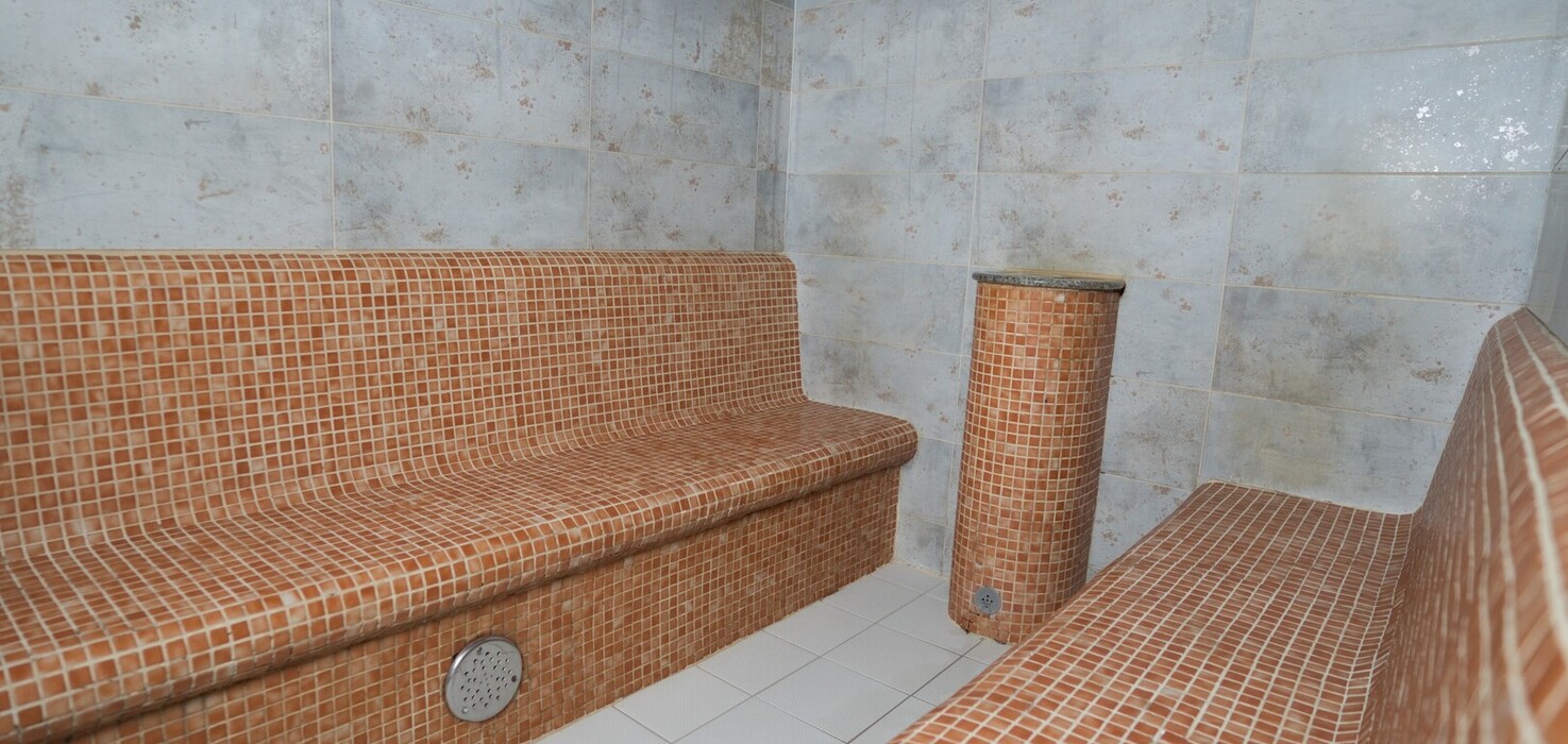 Przytulna sauna parowa w spa z podgrzewanymi ławkami i kolumną z brązowych mozaikowych płytek.