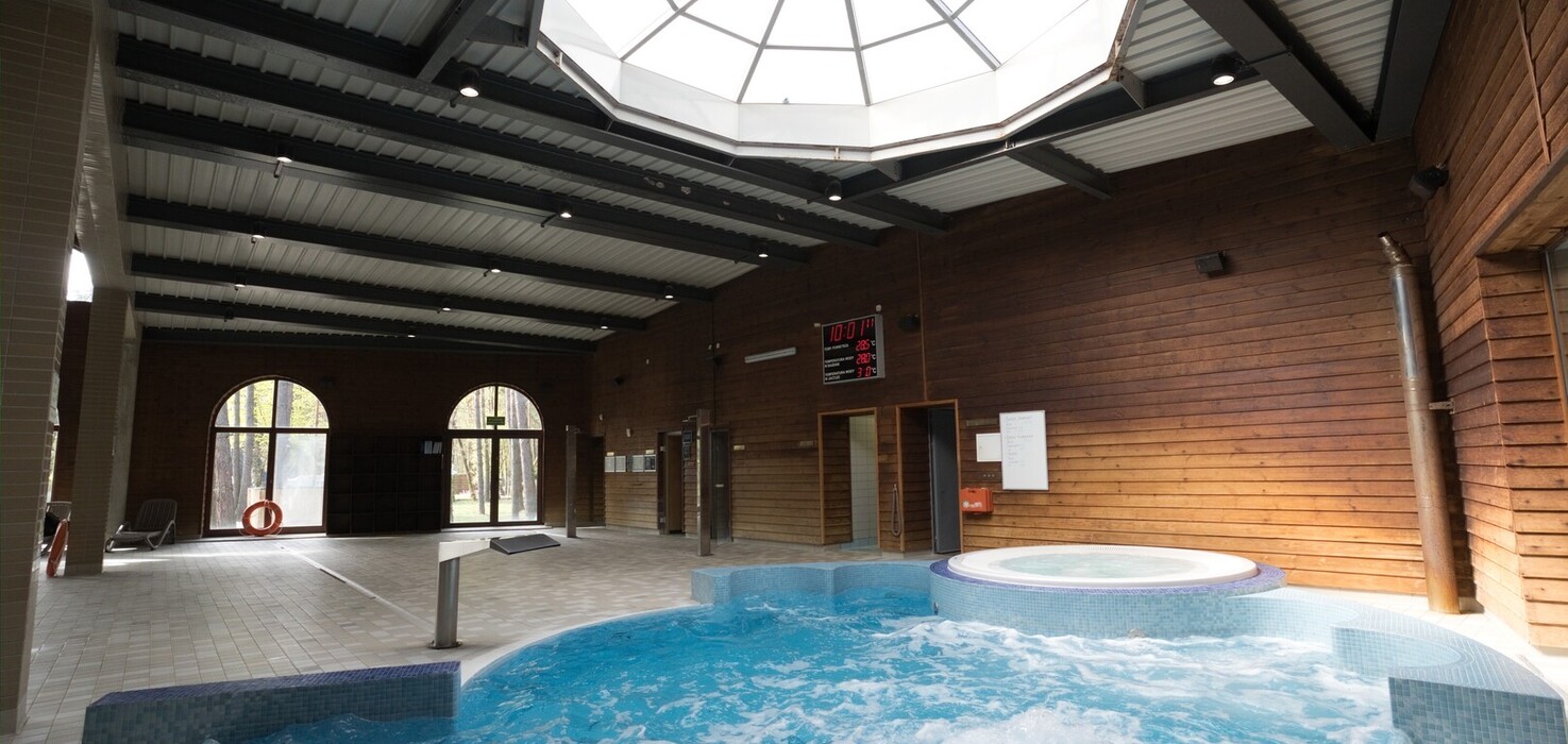 Wnętrze spa: jacuzzi i basen z hydromasażem, duży kopułowy świetlik, drewniane ściany i łukowe okna z widokiem na las