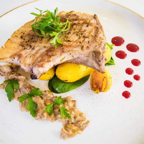 Grillowany filet na małych ziemniakach z kremowym sosem grzybowym, listkami szpinaku, natką i kroplami czerwonego sosu.