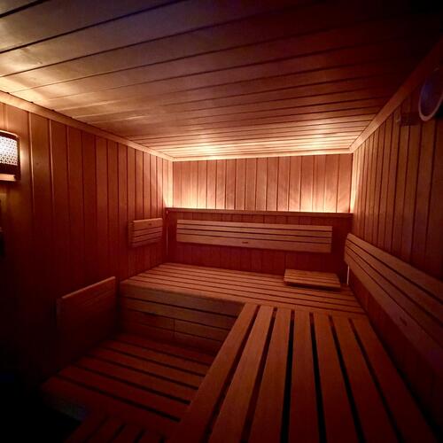 Sauna hotelowa z drewnianymi ławami, podświetlanym oświetleniem LED i nastrojną, ciepłą atmosferą relaksu