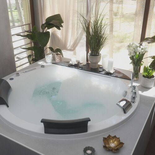 Jacuzzi z bąbelkami i podgłówkami w jasnym pokoju spa, udekorowane świecami i doniczkowymi roślinami