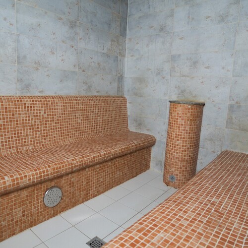 Przytulna sauna parowa w spa z podgrzewanymi ławkami i kolumną z brązowych mozaikowych płytek.