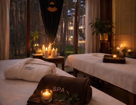 Przytulny salon spa z dwiema leżankami, zapalonymi świecami, ręcznikiem z napisem SPA i widokiem na sosnowy las przez duże okna