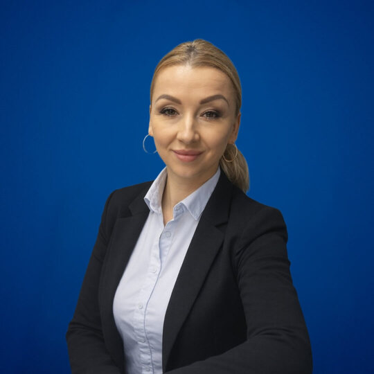 Przyjazna menedżerka recepcji hotelu w czarnym żakiecie i białej koszuli, na jednolitym niebieskim tle